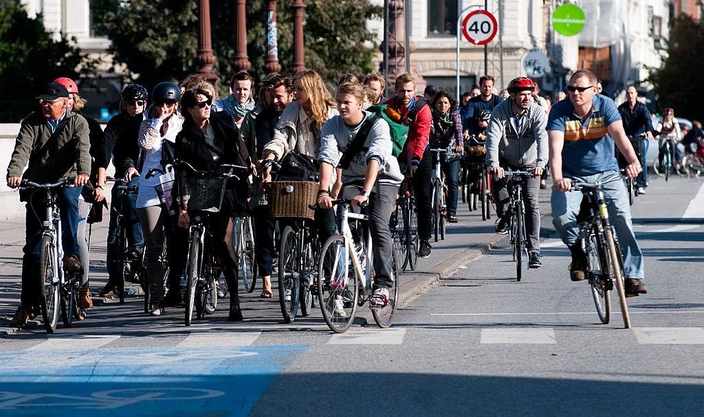 The photo shows a street packed with cyclists during daytime, all stopped in front of a traffic light, facing the camera.
