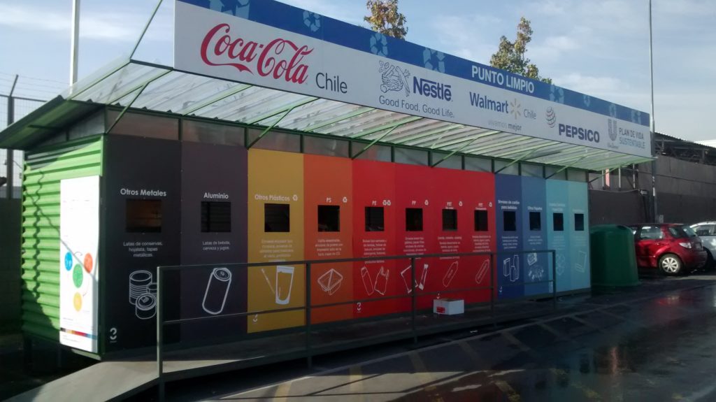 A foto mostra um Ponto Limpo, com várias repartições coloridas destinadas a receber diversos tipos de resíduos. 