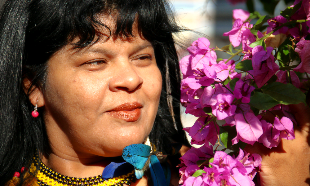 A black-haired woman, wearing an earring with a red bead, is looking happy, touching a bunch of flowers. 