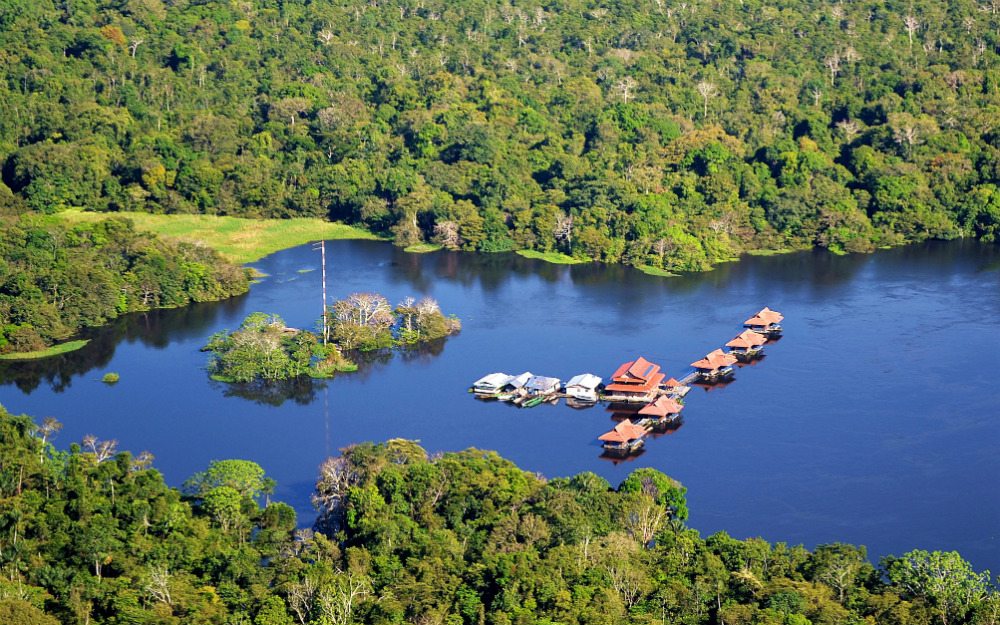 A view from above of some huts built in the middle of a river with a very green forest on its banks.