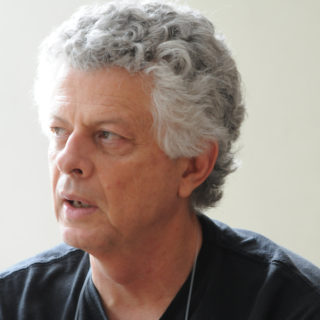 Foto de um homem de cabelos brancos com blusa preta.