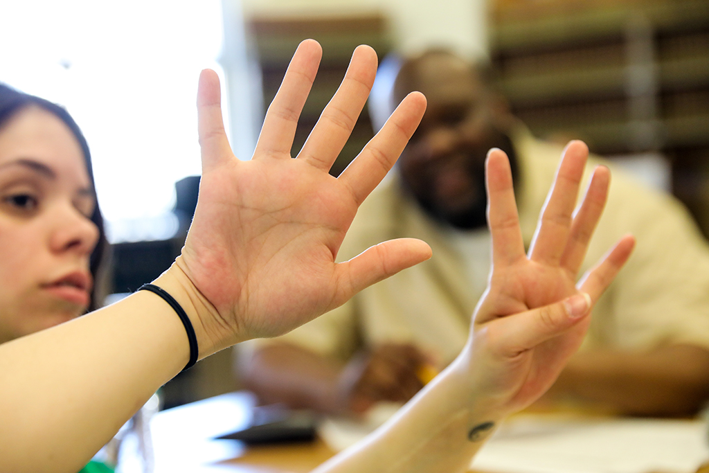 Plano cerrado de las manos de la voluntaria Laura (mujer, blanca, pelo lacio y negro). La mano derecha está abierta y la mano izquierda hace el signo del número 4.