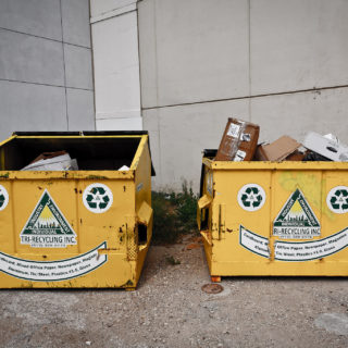 Two large, square metal dumpsters with trash in them. One is full, the other much less so. On the front of each dumpster are stickers arranged in a smiley-face shape.