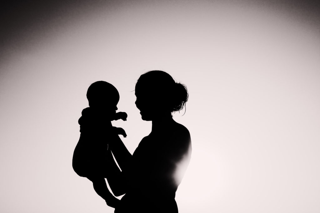 White background with the shadow of a woman who holds with both hands a baby in front of her face