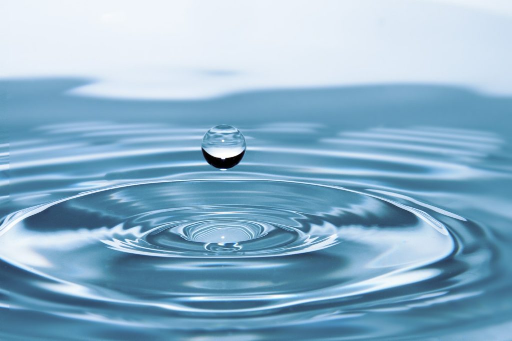 Close up of a drop of water falling in blue water, making ripples.